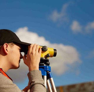 young man wearing hi-vis vest looks through surveying equipment