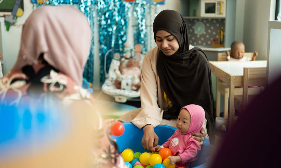 young girl with a practice baby doll in a ball pit 