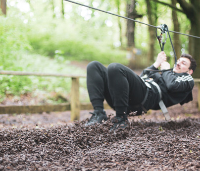 young man attached to rope via harness lands on bark ground