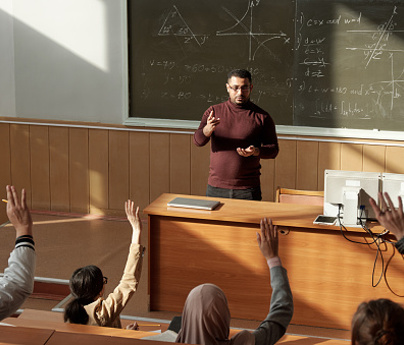 teacher stands at front of classroom in front of blackboard with equations