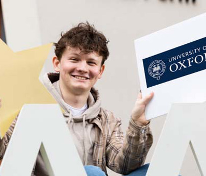 Morgan Grimshaw holding University of Oxford sign sat behind large As