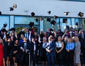 Group of graduates and staff throwing graduate hats into the air 