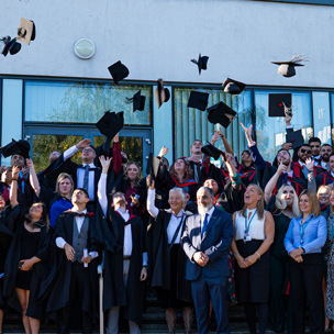 Group of graduates and staff throwing graduate hats into the air 