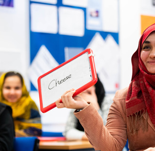 smiling student in headscarf in classroom holding sign with cheese written