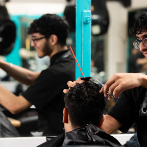 smiling barbering student cuts clients hair