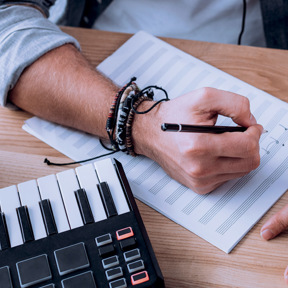 close up man writing music next to keyboard