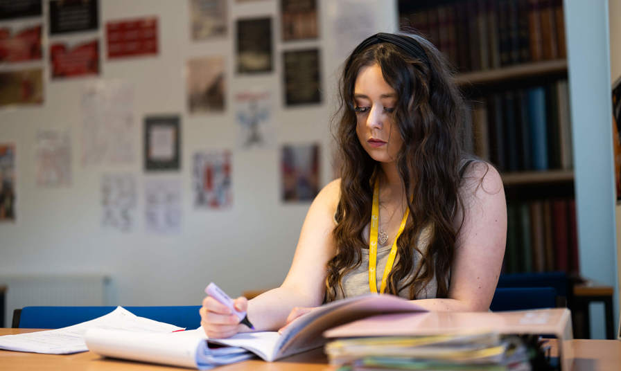 A girl studying and using a highlighter in a booklet