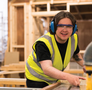 man wearing protective goggles and headphones operates joinery equipment
