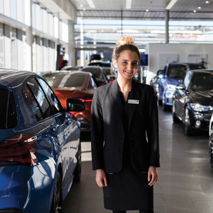 smartly dressed young woman stands in car showroom