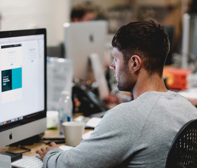 man sits working at mac in busy office