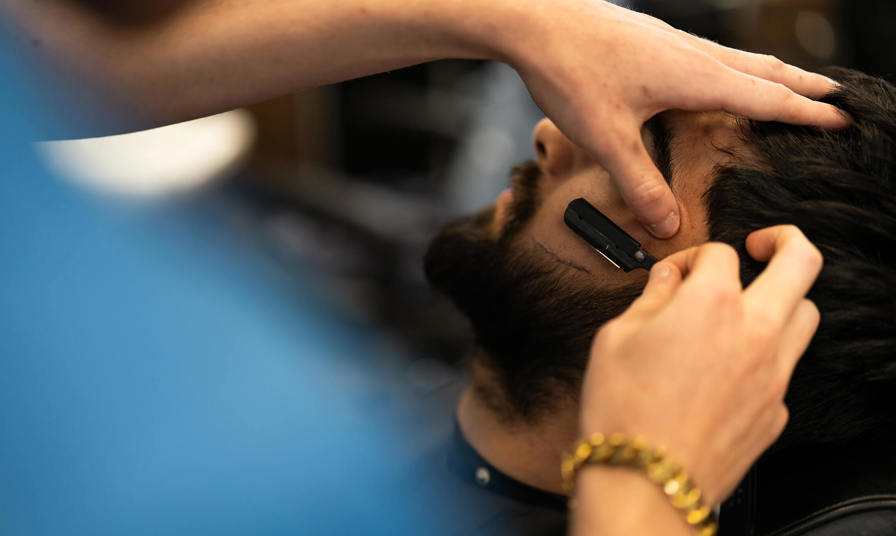 Student using a razor to shave someone's beard