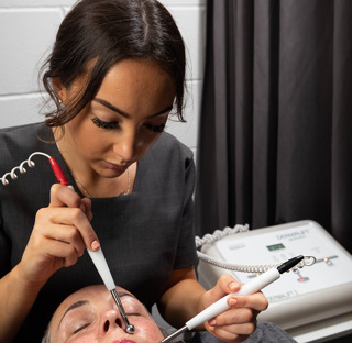 student beauty therapists using electronic beauty equipment of clients face