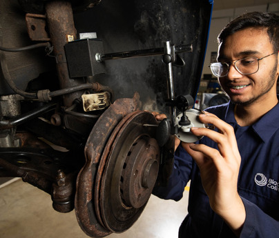 student in mechanics overalls looking at chassis of car