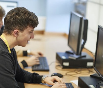 2 students smile working on laptop in brightly lit classroom