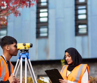 Students wearing hi-vis vests using surveying equipment on campus
