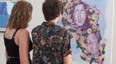 2 people look at painting of heads in flowers at art exhibition