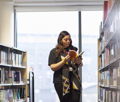 student looks at books in-between library shelves