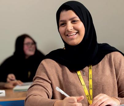 student wearing headscarf in classroom smiling doing work