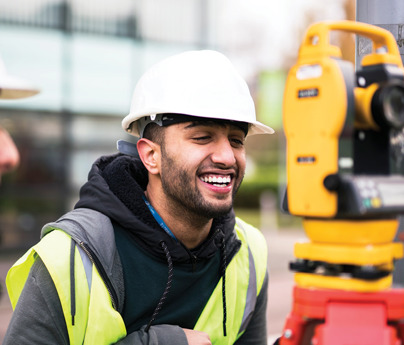 students in hard hats and high-vis vests smiling using surveying equipment