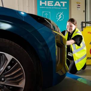 female student with hi-vis crouched down next to car and Hybrid/EV signs