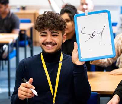 smiling student in classroom holds pen and board with soup written 