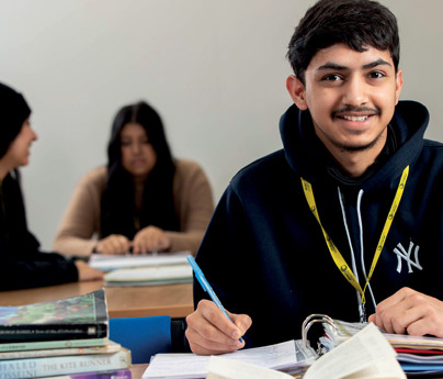 student with ring binder and books in classroom smiling to camera