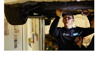 two students underneath a car doing mechanics in the HEAT Building. Image placed on a white background for sizing.