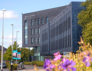 Beacon Centre building on campus at Blackburn College in sunshine. Purple flowers