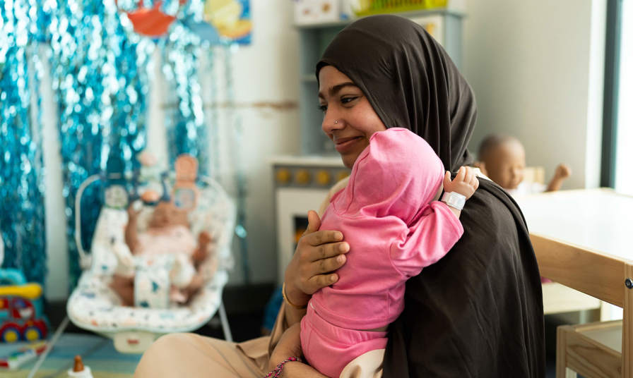 Young girl holding a practice baby doll and patting it on the back 