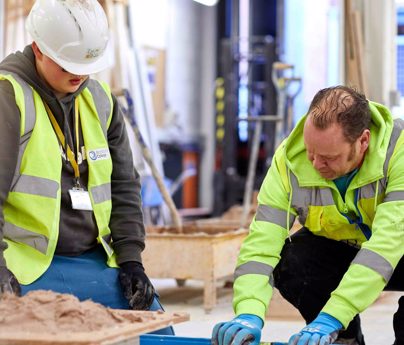 tutor helps bricklaying student level up a brick wall