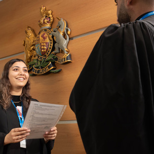 woman wearing black robes holding paper underneath crest on wall 