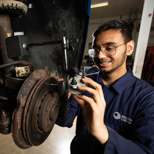 student examines car chassis in mechanic workshop