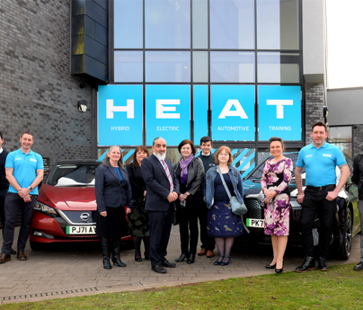 group of people stood in front of 2 cars and HEAT building Hybrid Electric Automotive Training sign