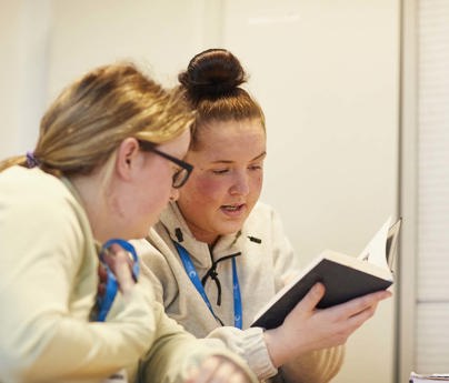 2 students look over a book together in classroom