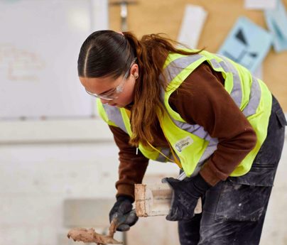 young woman using spirit level on brick wall in workshop
