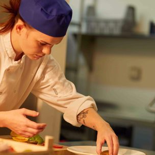 Student preparing food in a kitchen wearing a chef uniform.