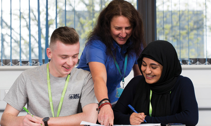 teacher leans over 2 students to show them something in a book