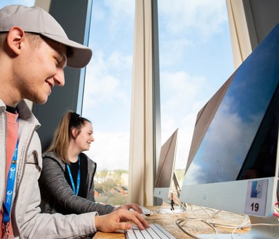 students smiling sat at mac computers in bright classroom