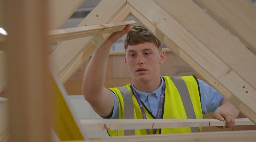 young man in hi-vis jacket surrounded by wooden beams