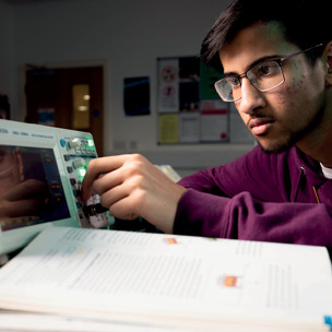 male student turning dials on oscilloscope with open text book