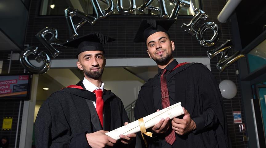 2 men in graduation cap and gowns holding scroll