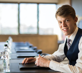 young man smartly dressed sits at boardroom