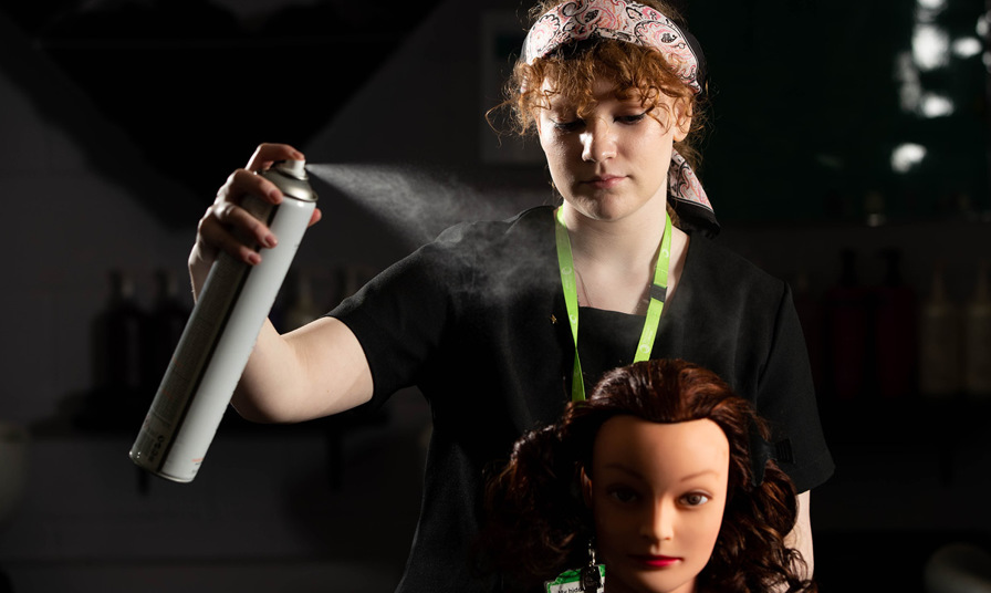 hairdressing student sprays hairspray onto mannequin