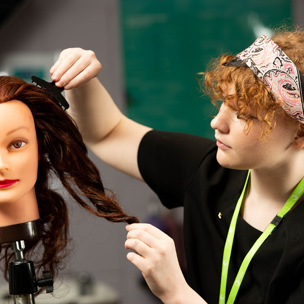 student hairdresser applies hair clips to mannequin 