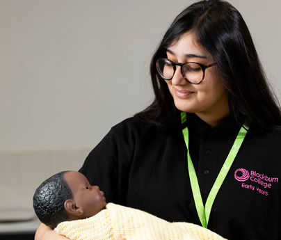 early years student holding dummy baby in arms