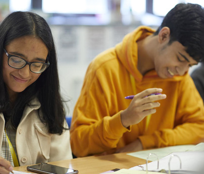closeup of 2 students sat at desk doing work smiling