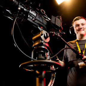 student smiling to camera whilst operating studio television camera
