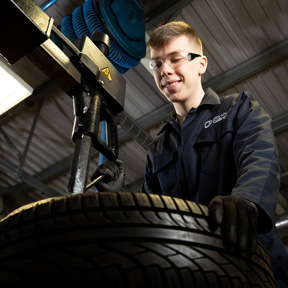 student in mechanics overalls looking at car tyre