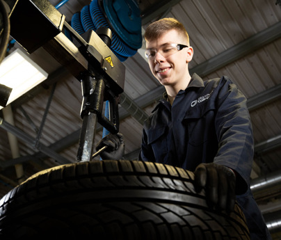 student in mechanics overalls looking at car tyre