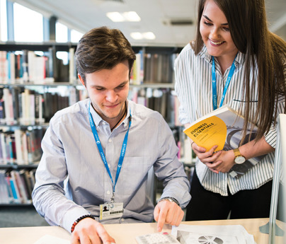 2 students working in library holding business textbook and working with calculator